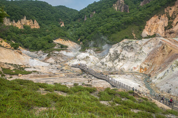 Tourists walking on wooden path through volcanic geothermal area in mountainous landscape at Noboribetsu Jigokudani Valley, Noboribetsu, Hokkaido, Japan