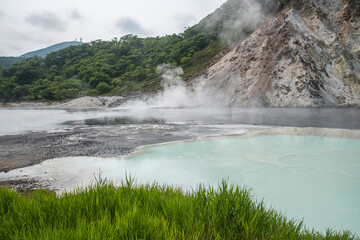 Volcanic hot spring steaming near mountain with green grass foreground at Oyunuma Pond, Noboribetsu, Hokkaido, Japan