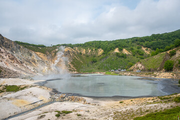Volcanic crater lake with steam and surrounding forest landscape at Oyunuma Pond, Noboribetsu, Hokkaido, Japan