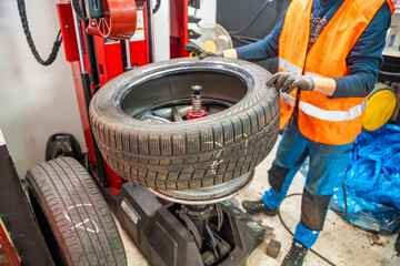 Fototapeta premium Mechanic replacing a rubber tire on the rim by hand after removal with a tire changing machine. Manual stage of seasonal tire replacement during winter preparation.