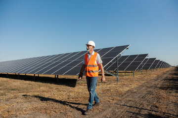 Senior Male Worker in Safety Gear Walking Near Solar Panels in a Rural Field