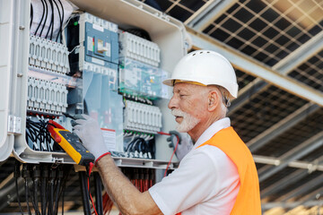 Senior Male Worker Inspecting Solar Panel Electrical Components for Maintenance at Solar Energy Industry Site