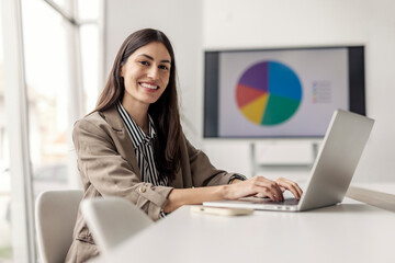 Fototapeta na wymiar Confident Businesswoman in Tan Blazer Typing on Laptop in Modern Office Fototapeta na wymiar Confident Businesswoman in Tan Blazer Typing on Laptop in Modern Office