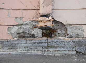 A broken drainpipe on a wall with crumbling plaster