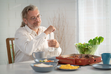 Elderly retired grandfather stay at home with painful face sitting alone on eating table in house. Depressed mature senior old man upset feeling unhappy. Lonely and missing his family at home	