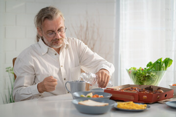 Elderly retired grandfather stay at home with painful face sitting alone on eating table in house. Depressed mature senior old man upset feeling unhappy. Lonely and missing his family at home	