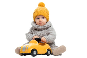 Cute baby in cozy sweater and hat playing with a yellow toy car on a white background.