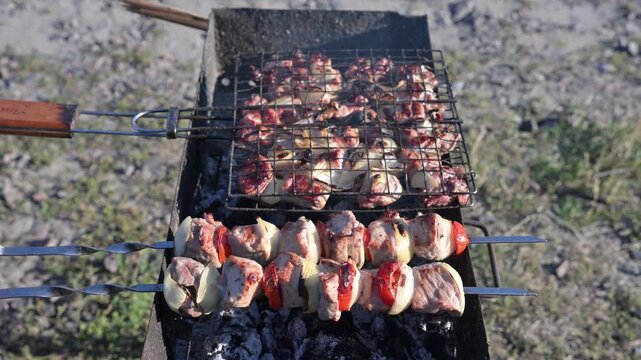 High-resolution 4K video showing the turning of a grill rack and skewers. The visual texture of browning meat, vibrant fire, and rising smoke is ideal for restaurant advertising and menu visuals.