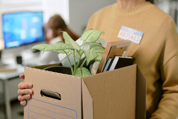 Middle aged Caucasian woman holding cardboard box filled with personal belongings and potted plant,...