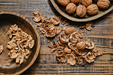 Various walnuts, broken shells, and walnut pieces on wooden table create a rustic kitchen scene