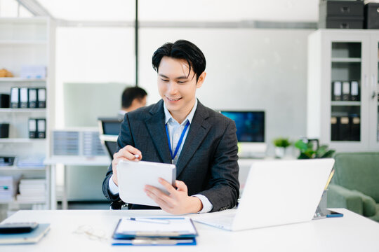 Confident Asian businessman using tablet and laptop in bright modern office, representing digital work, innovation - Powered by Adobe