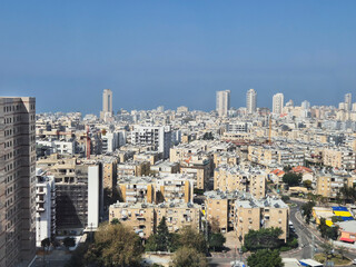 Urban view with densely packed buildings extending to sea horizon under blue sky, highlighting contrast between city and natural elements.