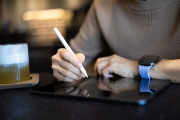 Close-up of a woman working on a tablet while sitting at a coffee shop.