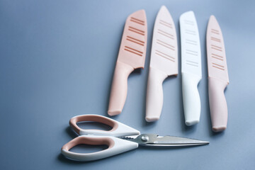 Modern pastel kitchen knives with silicone handles and plastic sheaths next to kitchen scissors on...