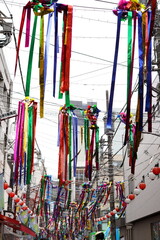 商店街の細い通りを縦に覆うように吊るされた色鮮やかでメタリックな輝きを持つ日本の七夕飾りの吹き流しの全景