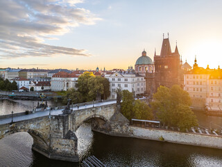 Obraz premium The sun sets over the historic Old Town Bridge Tower located by Charles Bridge in Prague. The river reflects warm colors as the day transitions to evening, highlighting the charming architecture.