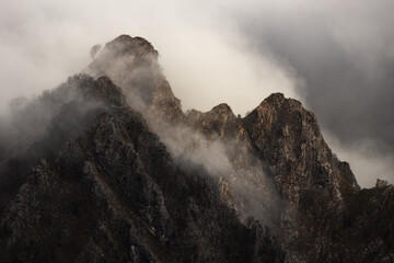 View of rugged mountain peaks shrouded in ethereal mist, rising dramatically against a cloudy sky, creating a sense of mystery and awe, Carrara, Tuscany, Italy.