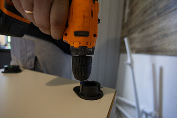 A man assembles a kitchen set. He holds a power drill, screwing the tool into a white cabinet, symbolizing home improvement, DIY projects, and renovations.