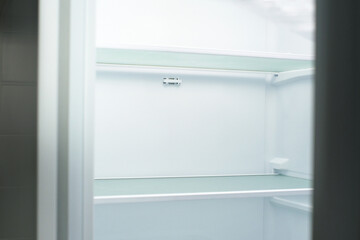 Modern white open refrigerator close-up with empty shelves, front view.