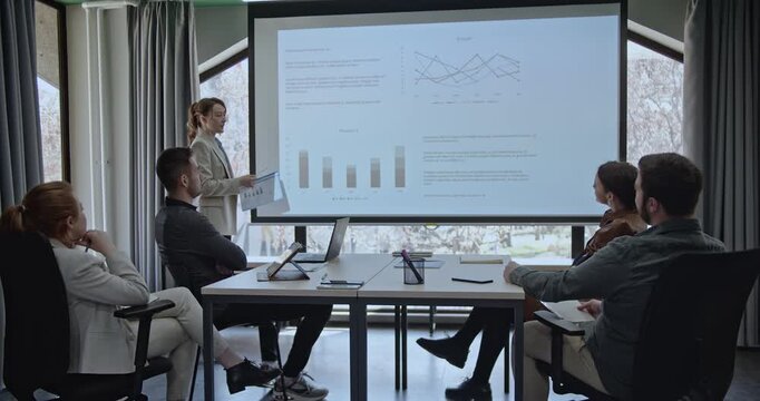 Business team in a meeting room analyzing graphs, charts, and reports projected on a screen. Collaboration, strategy, and data analysis are displayed during the presentation. - Powered by Adobe