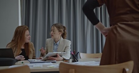 Two young businesswomen collaborate on a project using a tablet, discussing ideas and strategies in a modern office environment. - Powered by Adobe