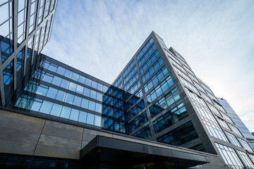 Glass high office building as headquarters of several companies and workplace for many people. Modern architecture in the city center in a business park. Detail of glass windows and reflection of clou