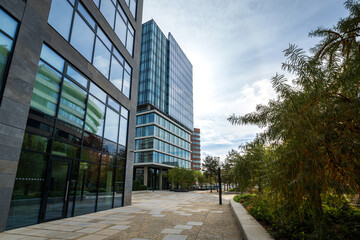 Center of office administrative buildings in the city. Modern architecture in a business park. Pedestrian walkway surrounded by greenery and trees.