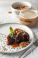 Chocolate spongy brownie cake served with walnuts and mint leaves on top and coffee close up. A piece of chocolate brownie cake