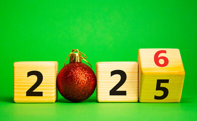 2026 New Year symbol. Businessman turns wooden cube and changes Year 2025 to 2026. Beautiful green background with christmas ball. Copy space. Business and 2026 happy new year concept