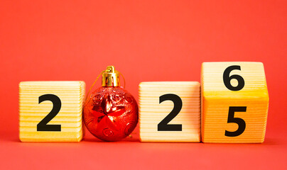2026 New Year symbol. Businessman turns wooden cube and changes Year 2025 to 2026. Beautiful red background with christmas ball. Copy space. Business and 2026 happy new year concept