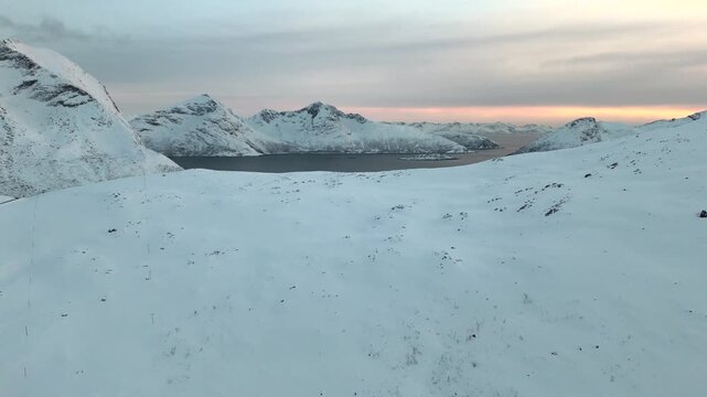 Aerial view above snowy mountain revealing fjords at sunset in the Artic