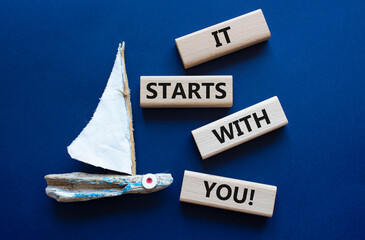 It starts with you symbol. Wooden blocks with words It starts with you. Beautiful deep blue background with boat. Businessman hand. Business and It starts with you concept. Copy space.