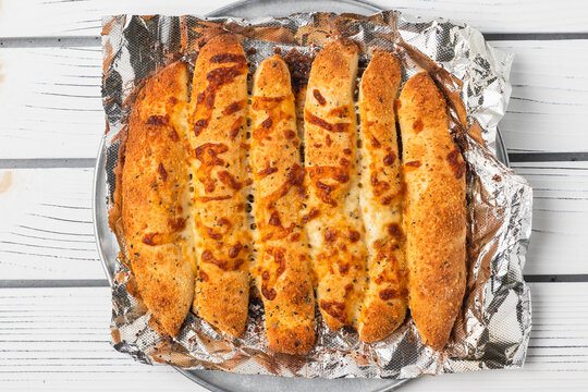 Freshly baked cheesy breadsticks served on foil over a metal pan. - Powered by Adobe