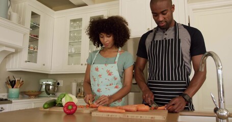 Chopping couple wearing aprons slicing carrots and peppers on kitchen island, with wooden boards