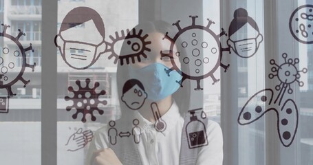 Standing Asian woman wearing blue mask behind glass partition, crossing arms with virus icons