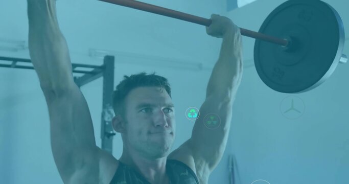 Lifting muscular male pressing barbell with plates overhead in gym with metal squat rack and lights