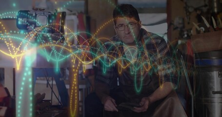 Craftsman in leather apron examining metal tool in busy workshop, with camera, digital waveforms