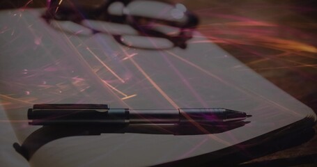 Lying metal pen without cap on blank notebook at wooden study desk, with eyeglasses, light streaks