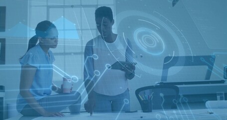 Collaborating women reviewing project at office desk, with tablet and coffee cup amid tech overlay