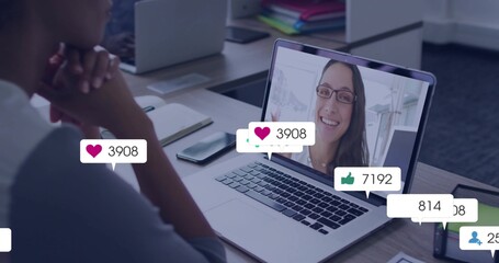 Viewing male in gray shirt clasping chin in office, with laptop showing smiling coworker with icons