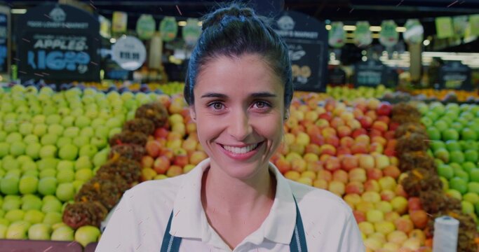 Standing store clerk wearing white tee and apron organizing apples in produce section, with signage
