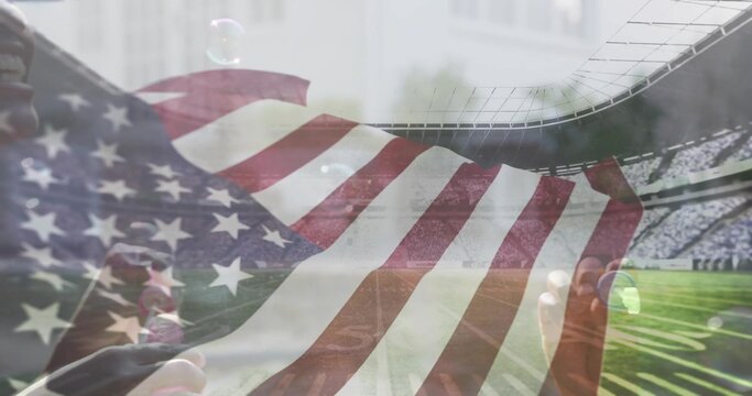 Stretching mother-son duo in sportswear holding ends on field at stadium, with large American flag - Powered by Adobe