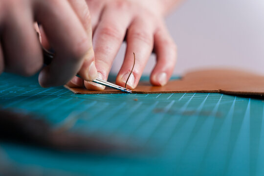 Trimming leather edge with tool. Artisan trims leather edges with precision tool, refining the cut. Craftsman refines leather edges with trimming tool, ensuring smooth curves and clean lines.
