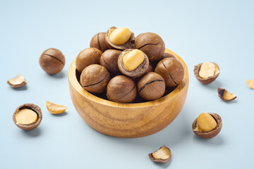 Macadamia nuts with shell in wooden bowl with broken macadamia on blue background