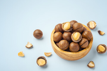 Macadamia nuts with shell in wood bowl with broken macadamia on blue background, top view