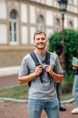 Fototapeta premium Smiling student holding backpack straps on university campus