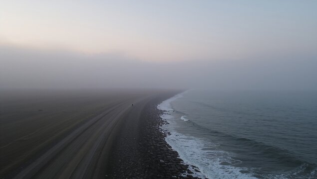 Curving shoreline separating sandy gravel beach from waves at misty dawn, with pebble breakwater