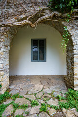 Naklejka premium old stone wall with arch covered by green ivy and window, close up of beautiful and cozy architectural details