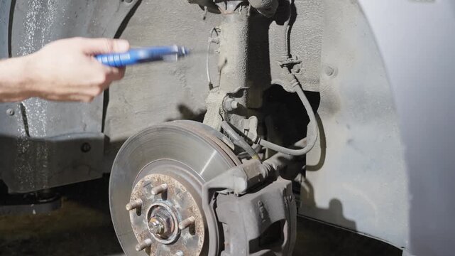 Man blows dirt off strut, area around rear wheel of car with air compressor and air gun, close up