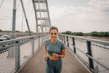 Young sporty woman running on the bridge in the city